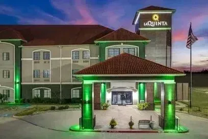 Burleson Electrician - A La Quinta hotel at twilight with green-lit entrance, an American flag, and a clear sky transitioning from blue to pink tones.