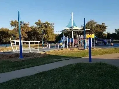 Burleson Electrician - Modern playground featuring colorful equipment, blue shade structures, and surrounding trees under a clear blue sky.