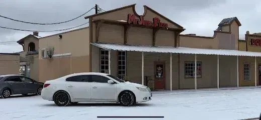Burleson Electrician -A white car is parked on a snowy street in front of a building with a sign reading