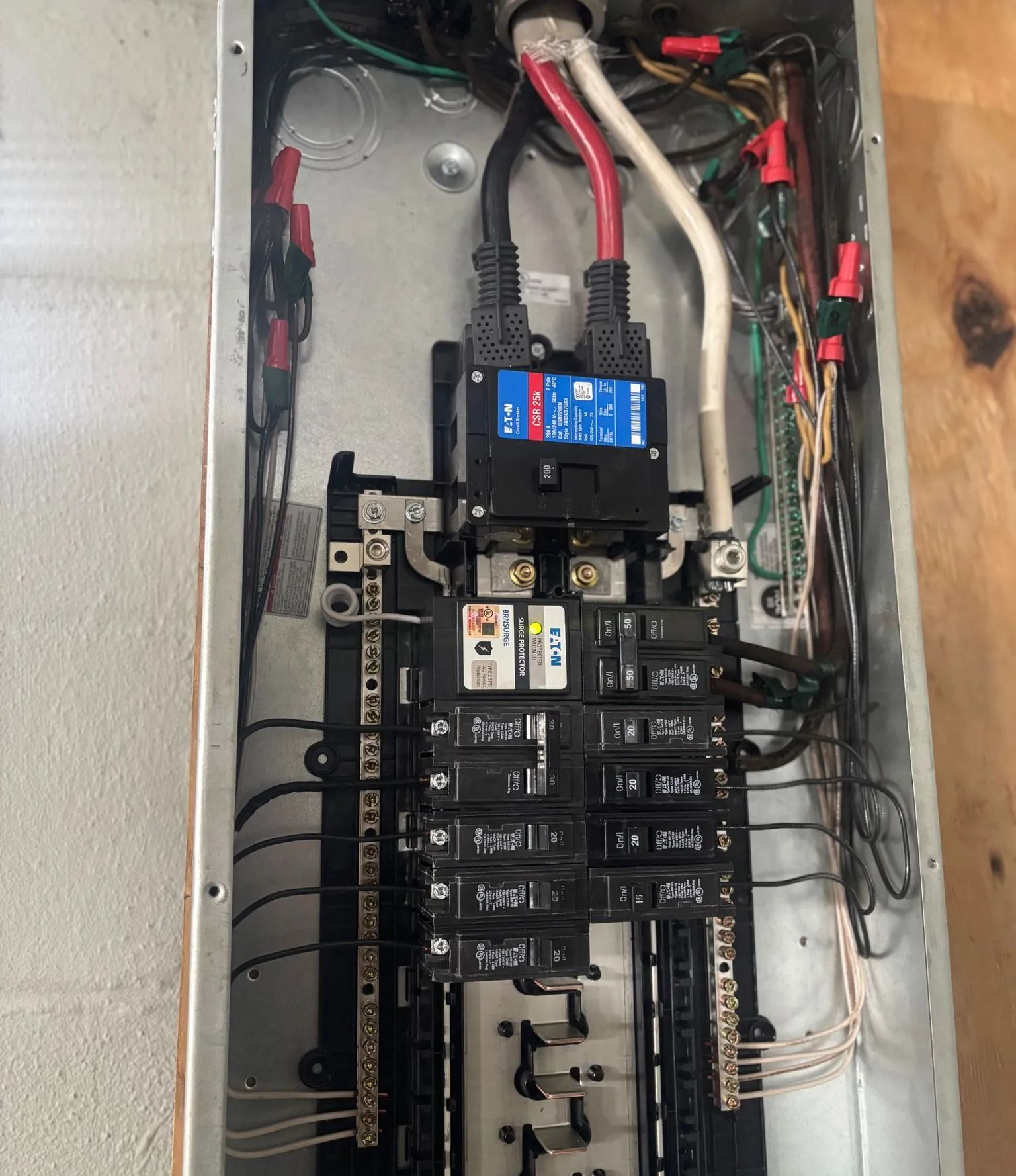 Open electrical breaker panel with wires, circuit breakers, and a blue device at the top.