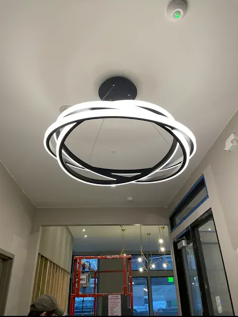 A bathroom with a lit ceiling light and marble tile. A shelf with toiletries is visible.