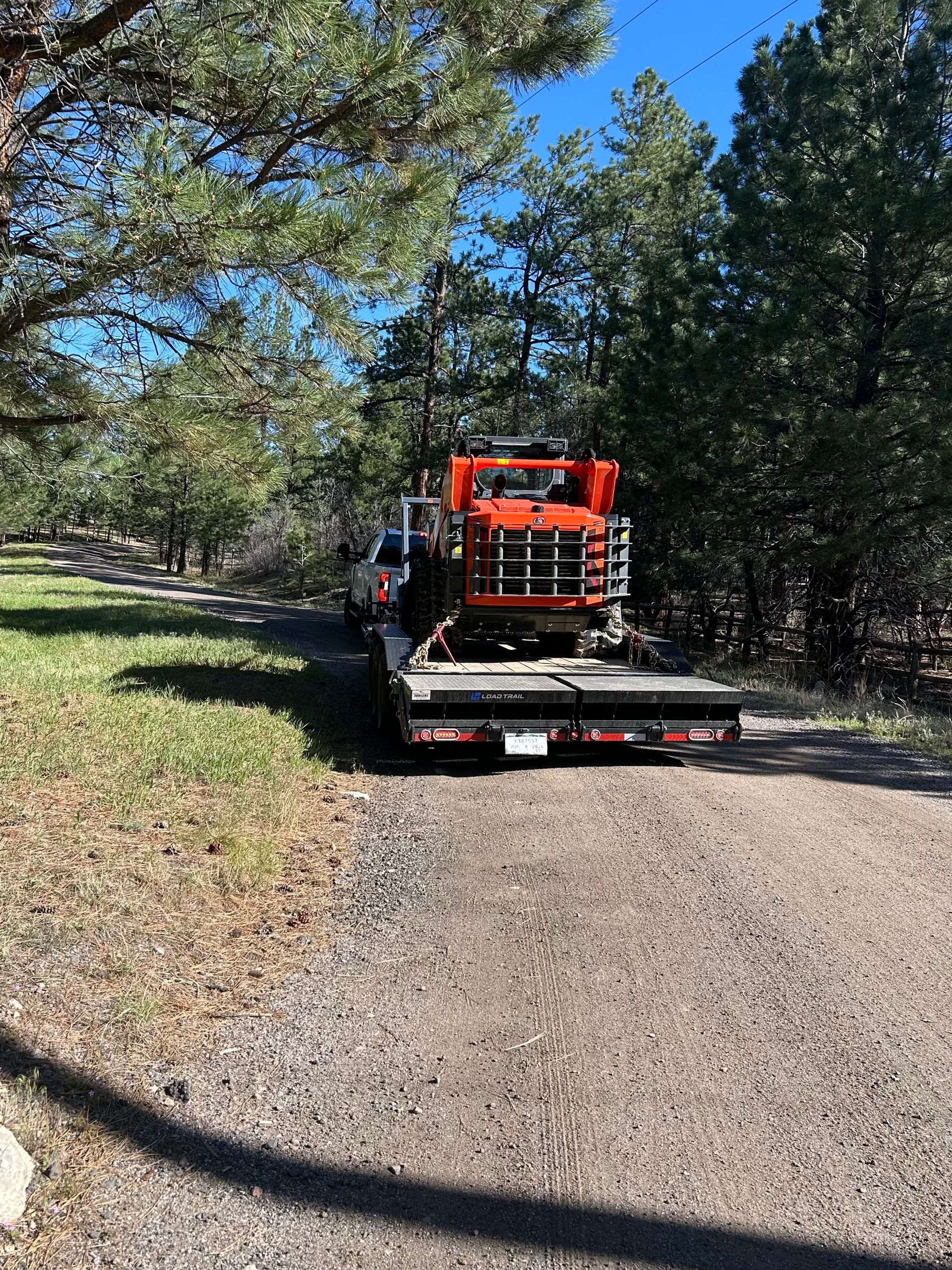 Flatbed truck carrying orange equipment on a gravel path in a wooded area