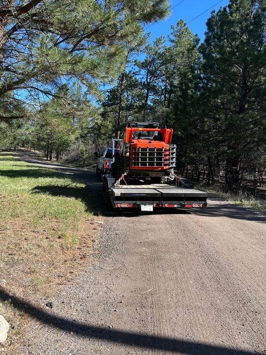 Flatbed trailer carrying orange equipment on a gravel road in a wooded area