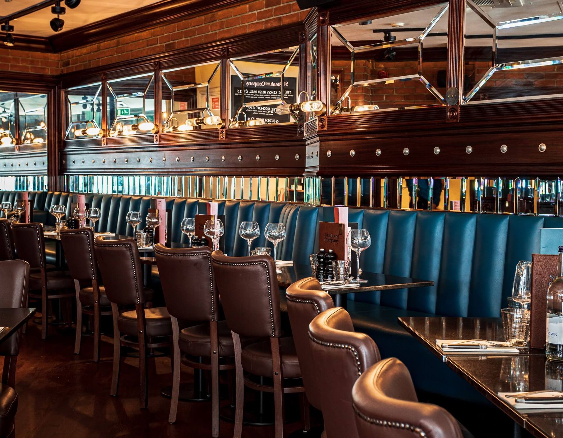 Restaurant interior with brown leather chairs, blue booths, mirrors, and tables set for dining.