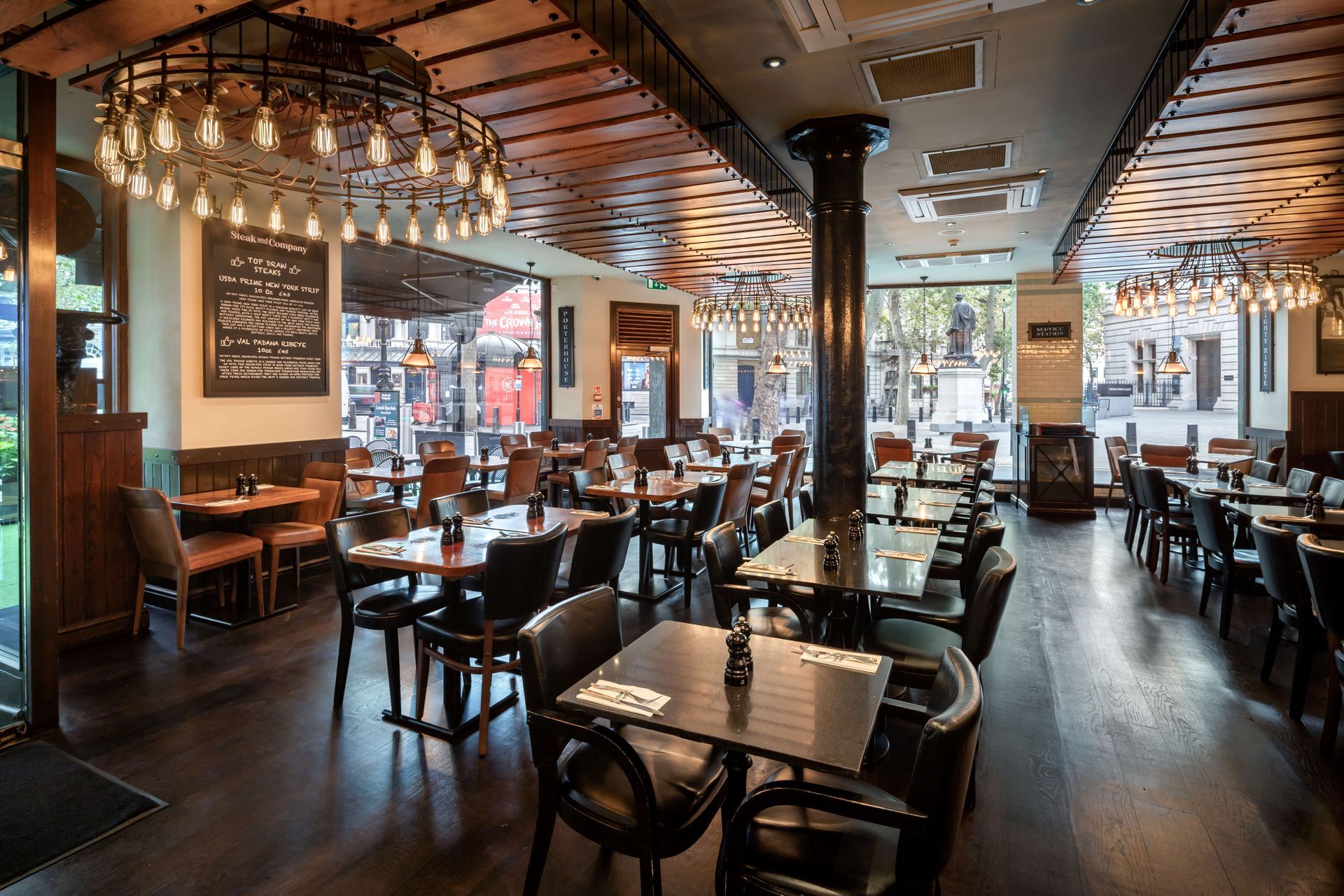 Interior of a restaurant with tables, chairs, dark wood floors, and large light fixtures.