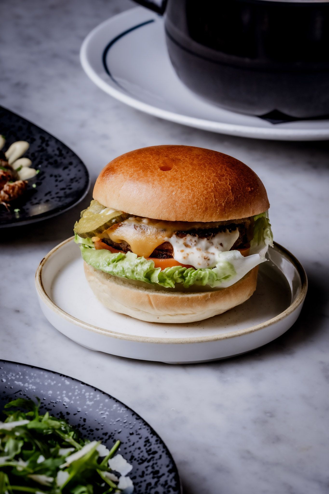 Hamburger on a small plate with side dishes, set on a marble surface.
