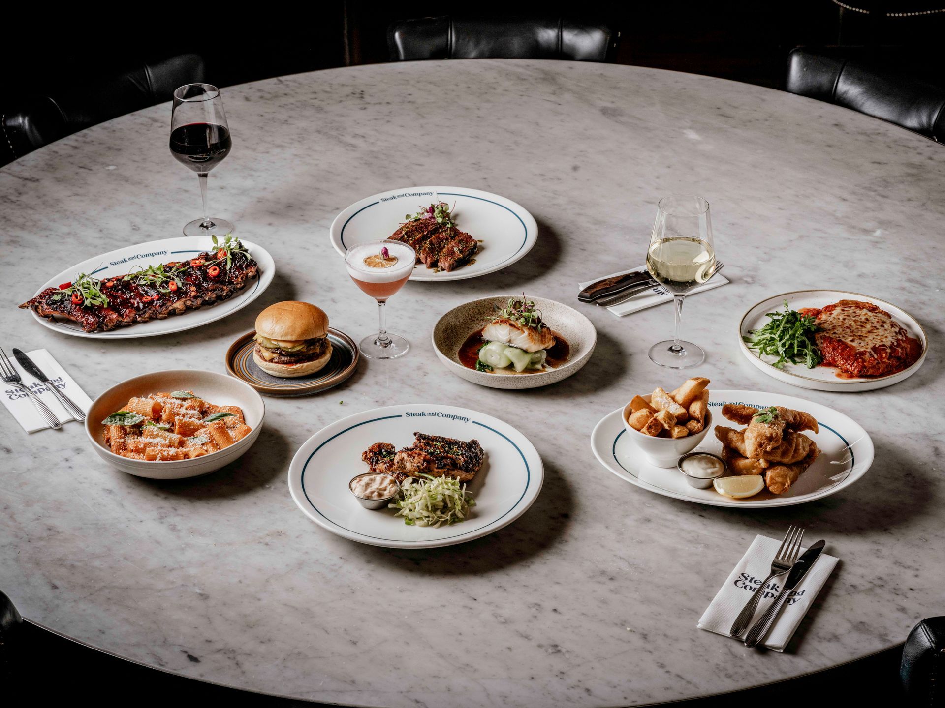 Main dishes with two glasses of wine on a light marble table.
