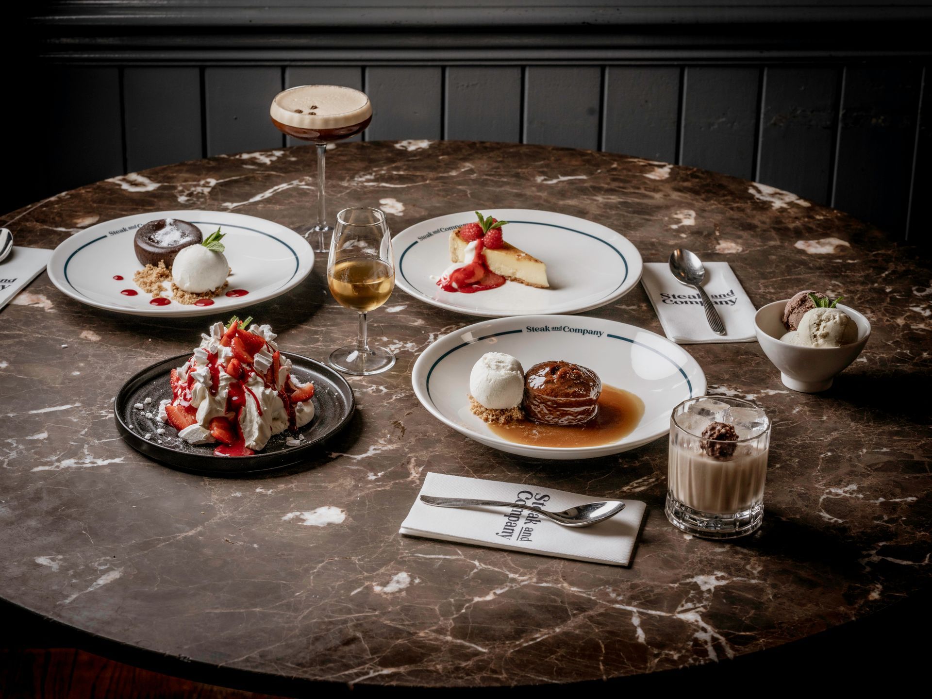 Desserts with a dessert wine and a cocktail on a dark marble table.