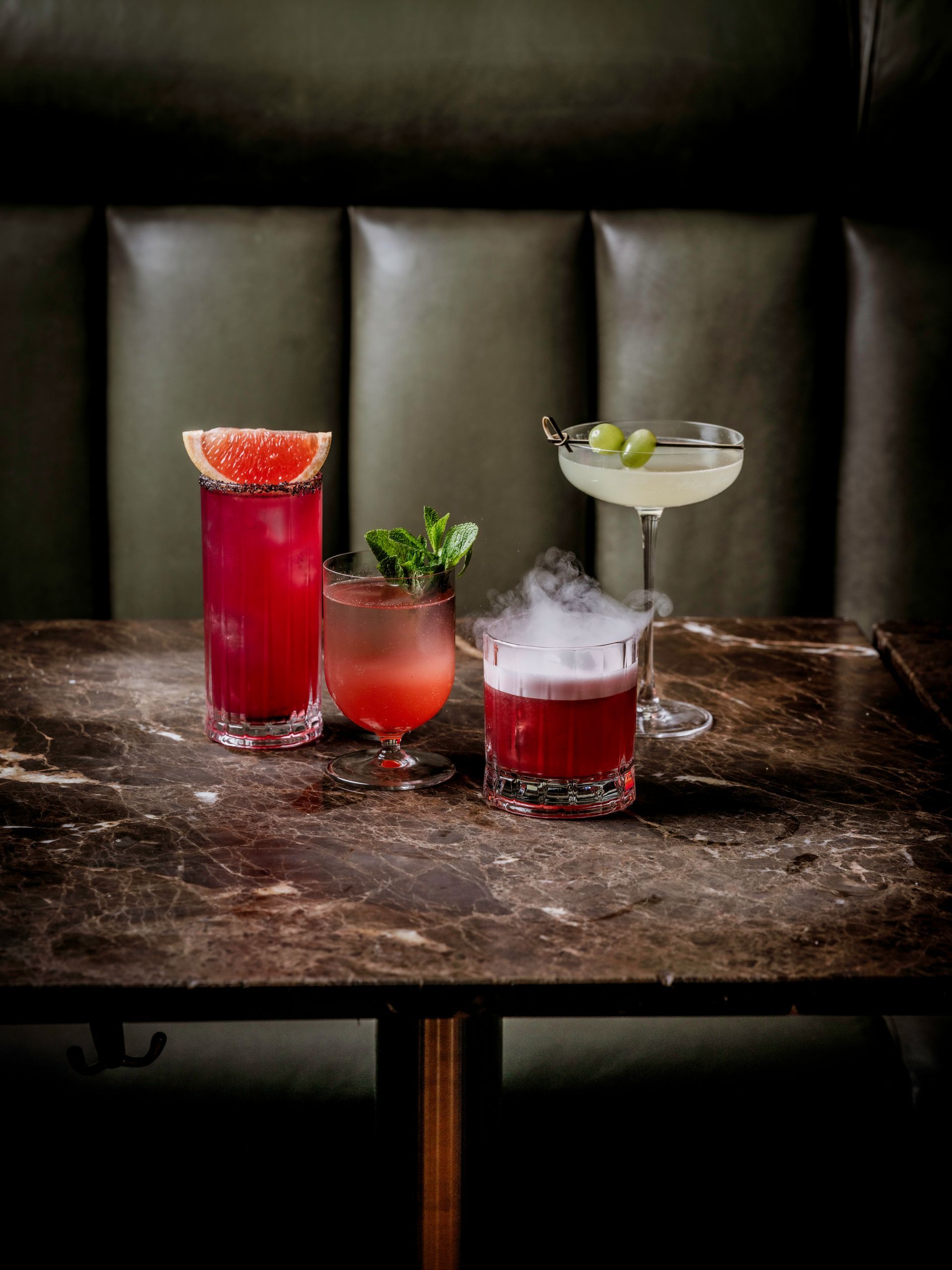 Four cocktails, one with a popped bubble on a dark marble table.
