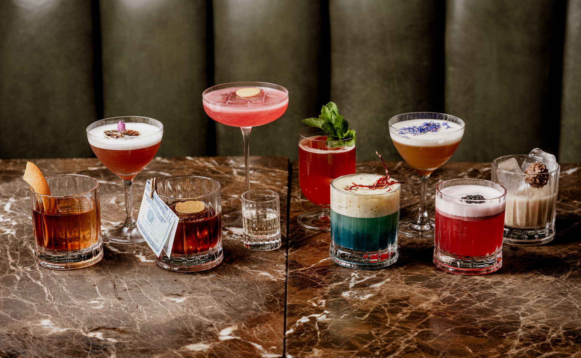 Four cocktails, one with a popped bubble on a dark marble table.
