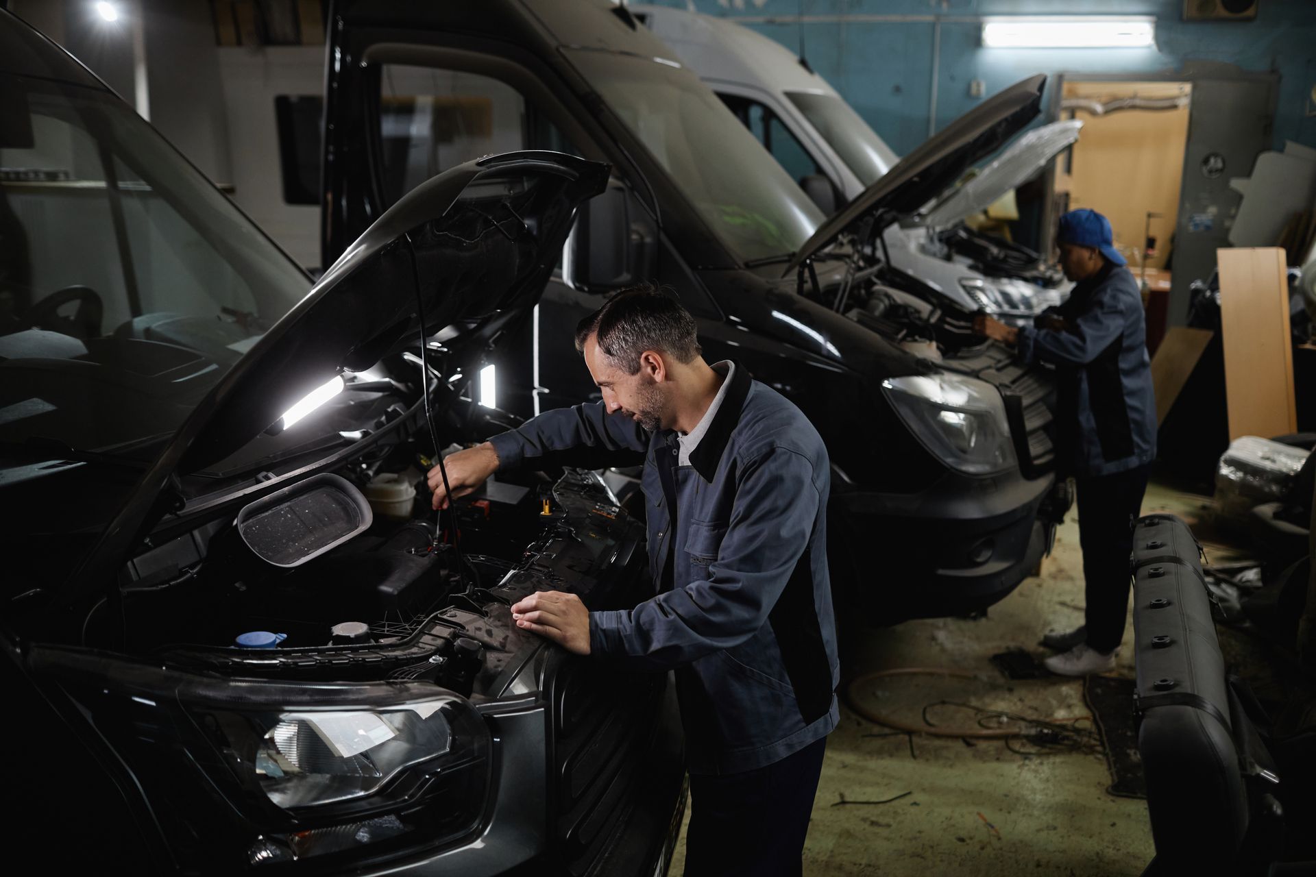 Side view of two car mechanics repairing vans and trucks in a garage shop. Side view of two car mechanics repairing vans and trucks in a garage shop.