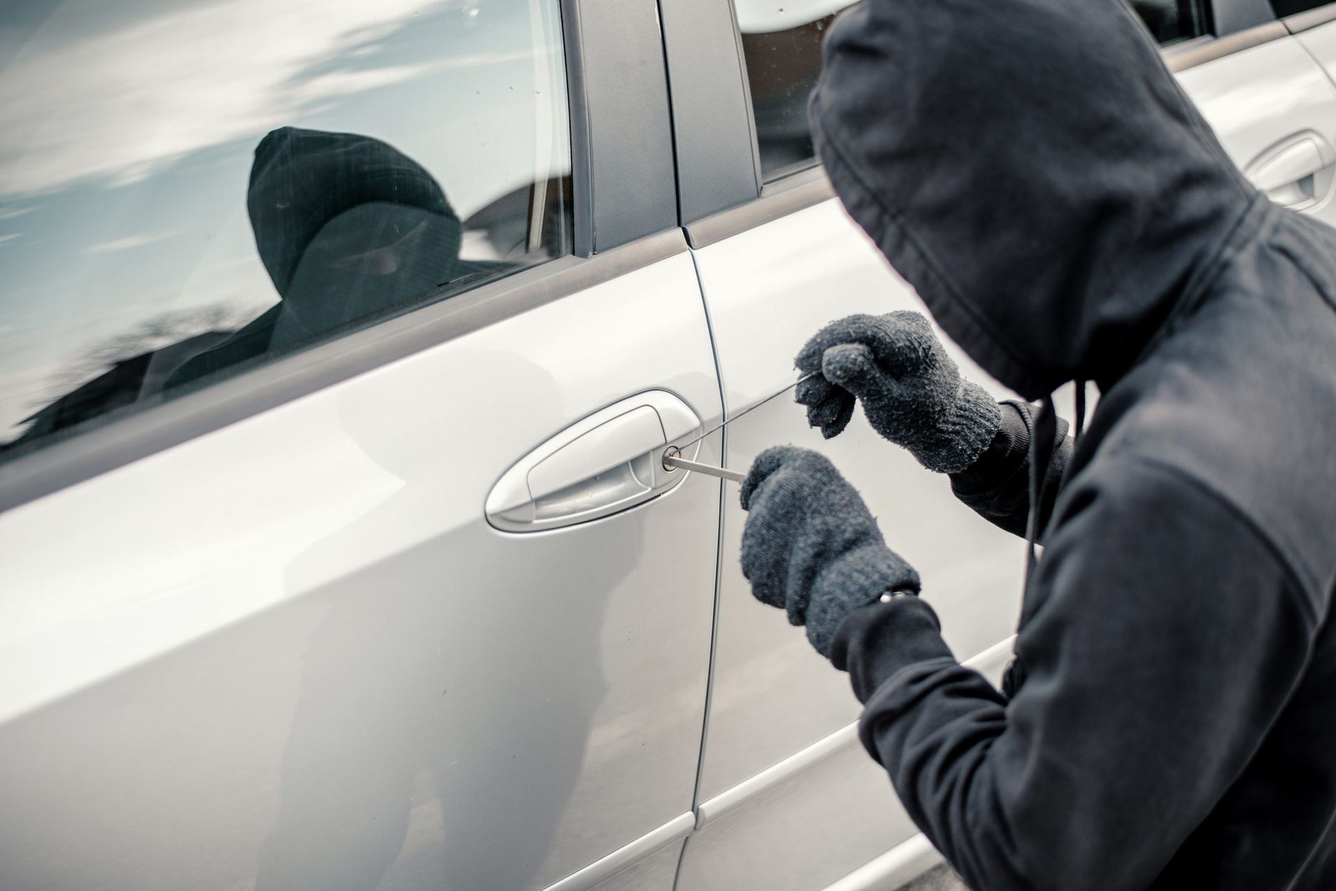 Man stealing a car — Mildura, VIC — United Panel Works Person in a black hoodie and gloves using a tool to break into a silver car.
