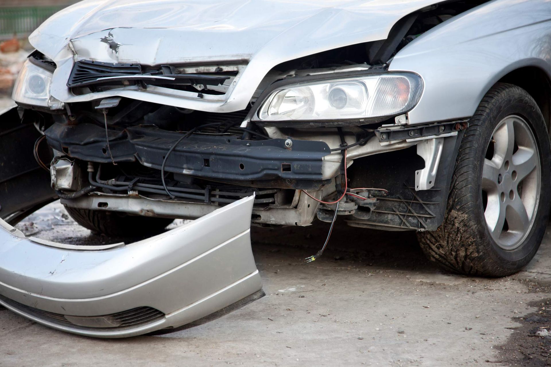 Front part of a damaged car — Mildura, VIC — United Panel Works Silver car with significant front-end damage; bumper detached, crumpled hood, headlight exposed.
