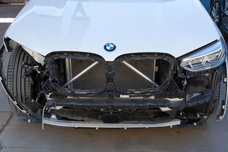 White BMW with front bumper removed, revealing radiator and supports.