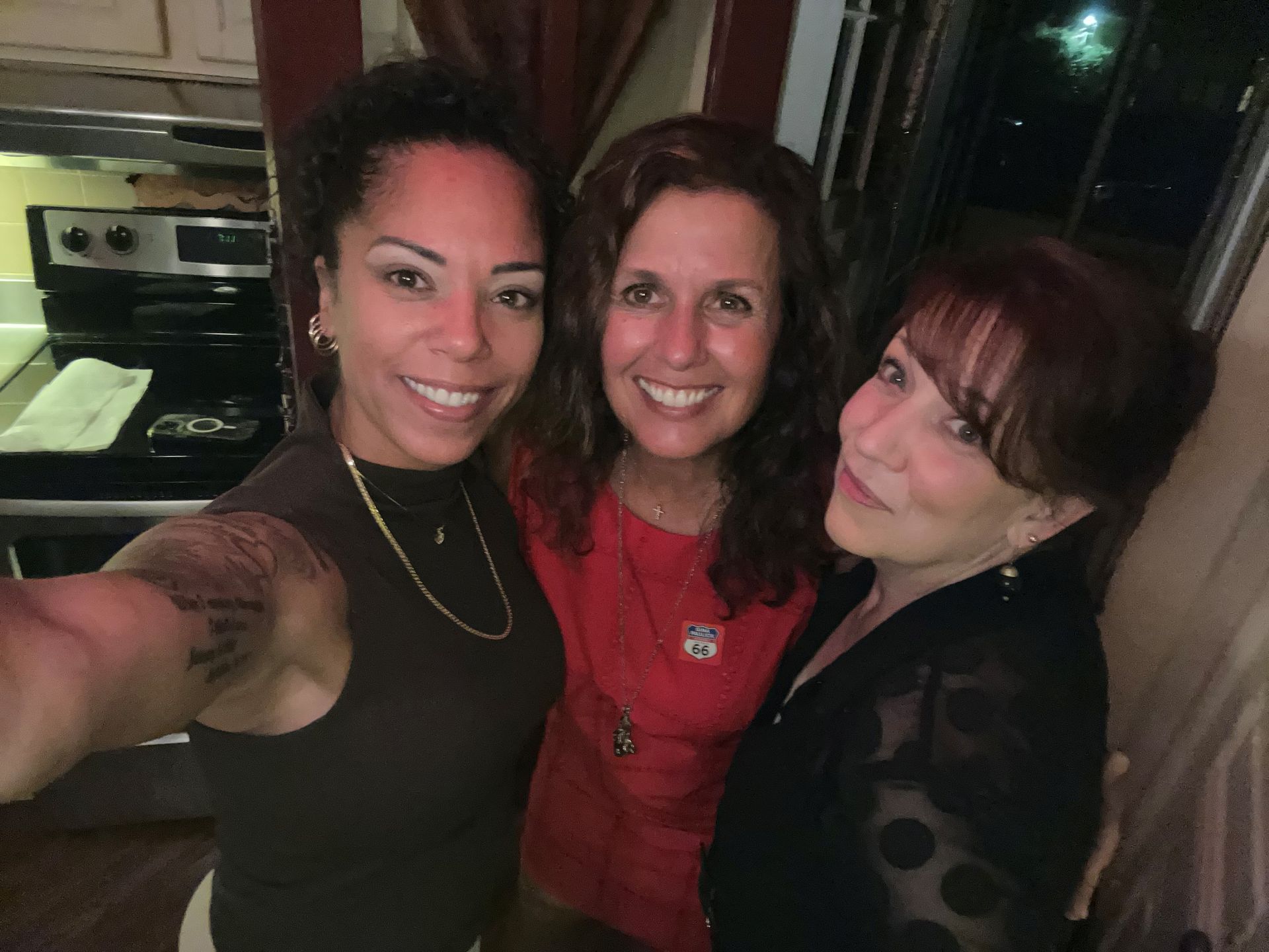 Three smiling women posing for a selfie in a dimly lit room.