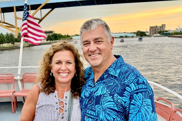 Smiling couple on a boat at sunset with an American flag and city skyline in the background