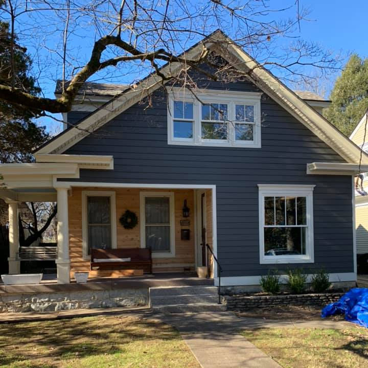 A two-story blue house with white trim, a porch, and wood-paneled accents under a clear blue sky.