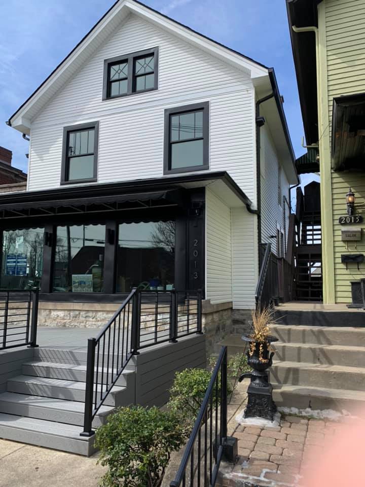 A two-story white house with black trim, a gray front porch with black railings, and stone foundation steps.