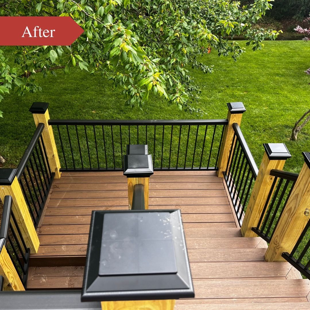Wooden deck with black railings, stairs, and a table overlooking a green backyard.