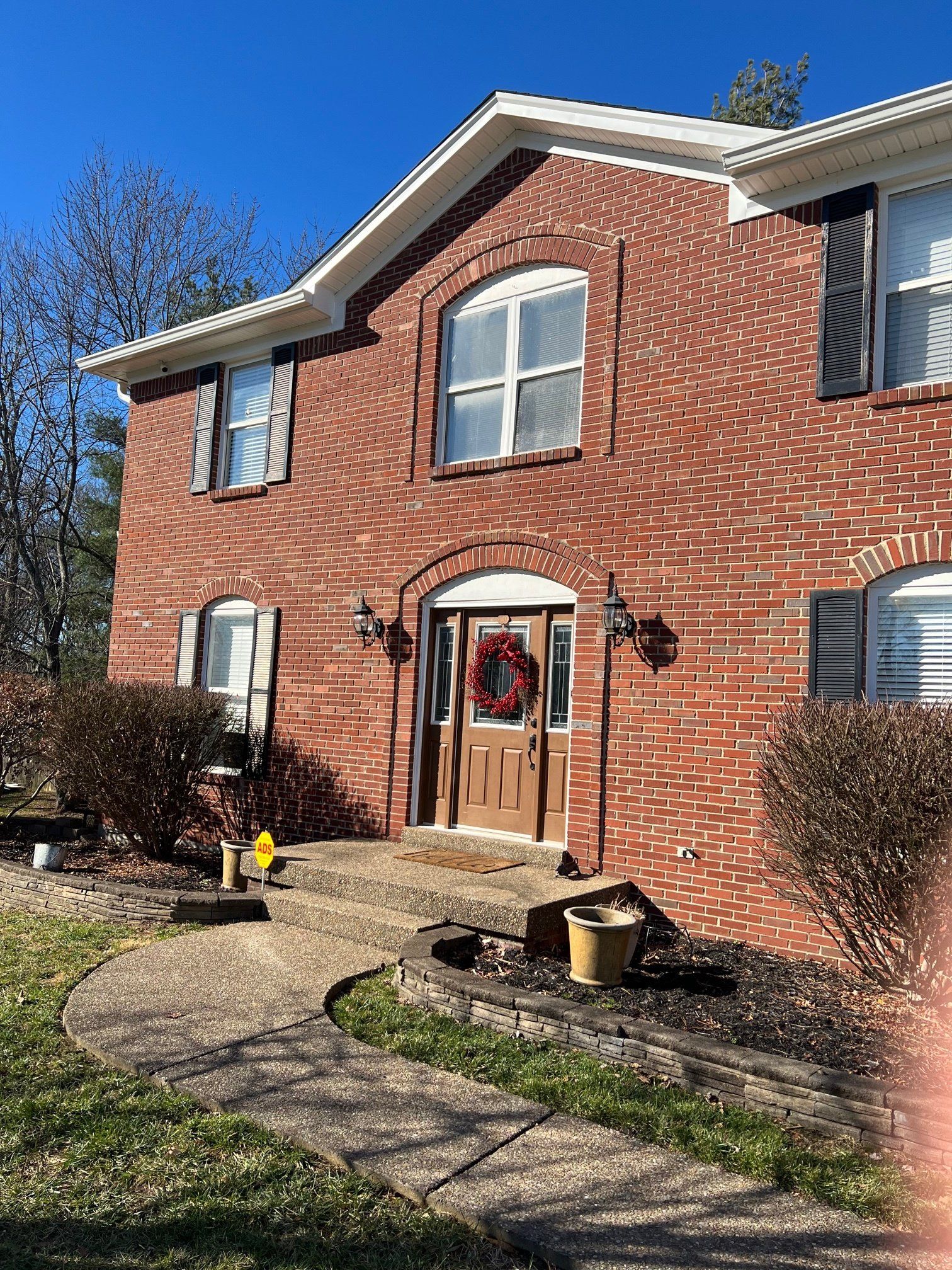 A two-story red brick house with a arched entryway, a wreath on the door, and a stone walkway leading to the entrance.