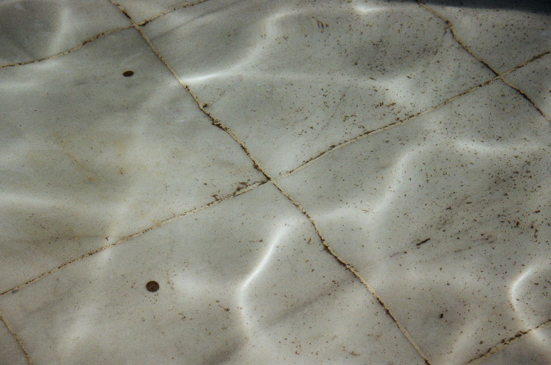 Sunlight ripples refract through shallow water onto the textured, light-colored floor of a pool or fountain.