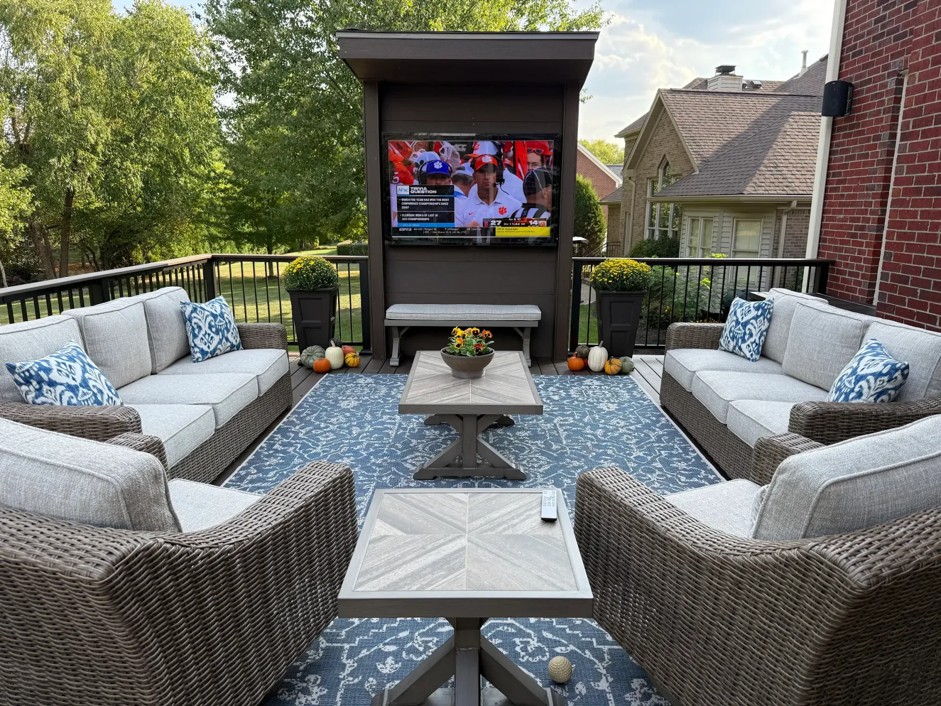 Outdoor patio seating area with wicker couches, a central table, and a wall-mounted TV on a deck.