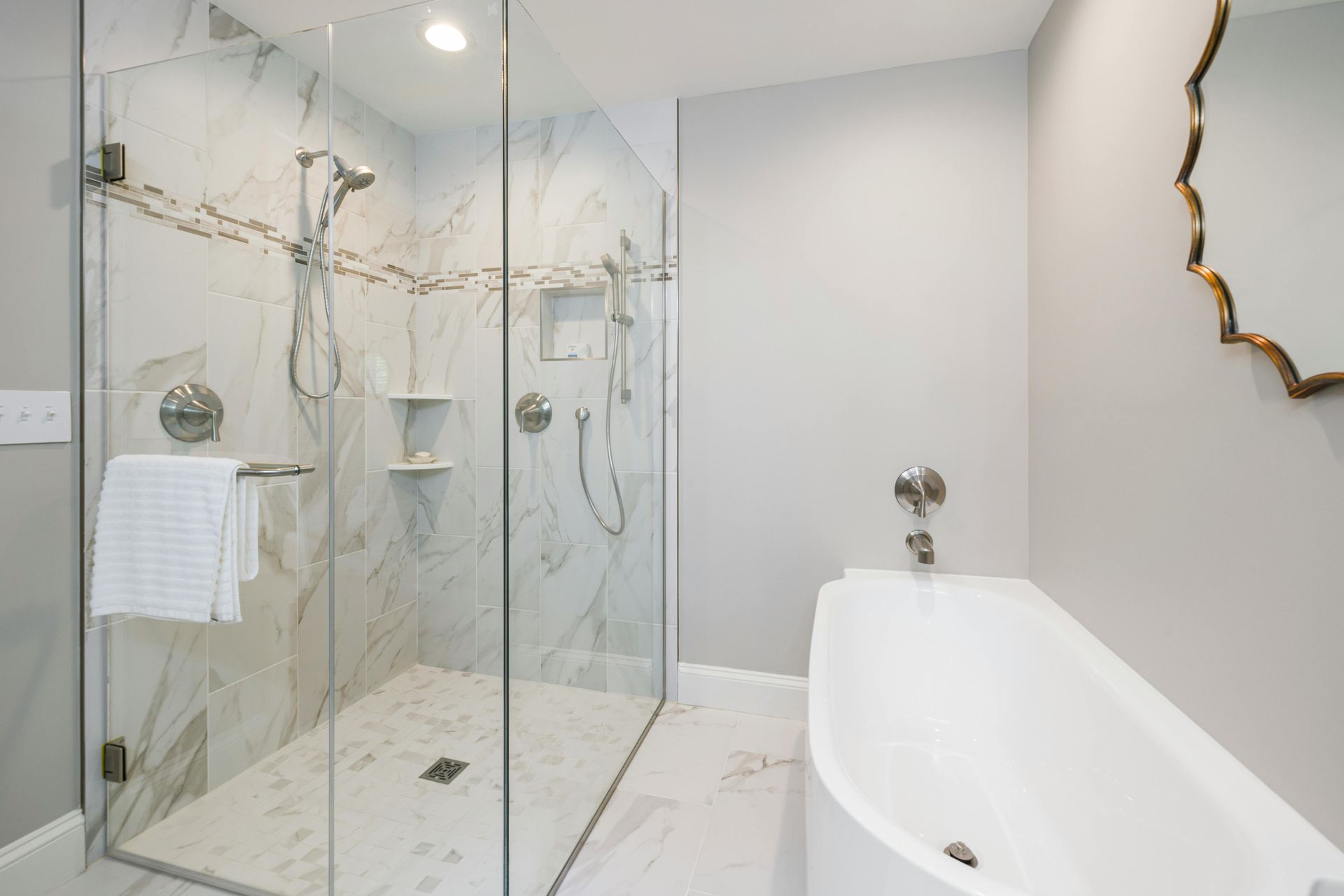 A modern bathroom featuring a white soaking tub next to a large glass-enclosed walk-in shower with marble tile walls.
