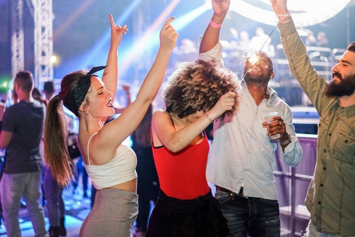 A group of people are dancing at a concert with their arms in the air.