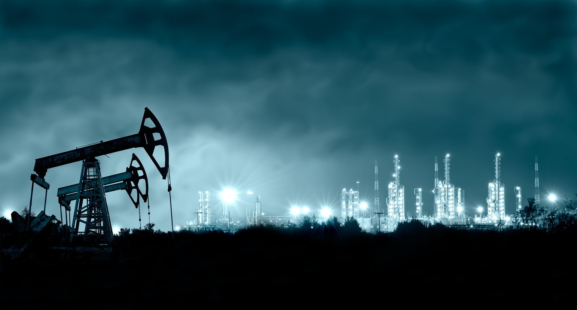 A silhouette of an oil pump in front of an oil refinery at night