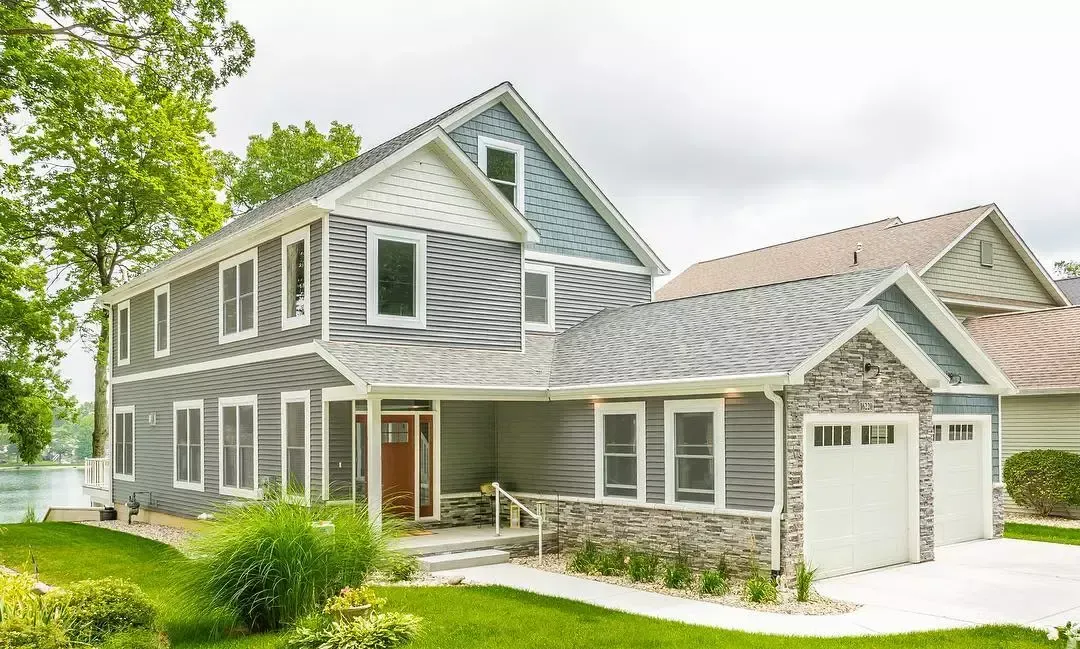 A large house with a lot of windows and a garage is sitting on top of a lush green lawn.