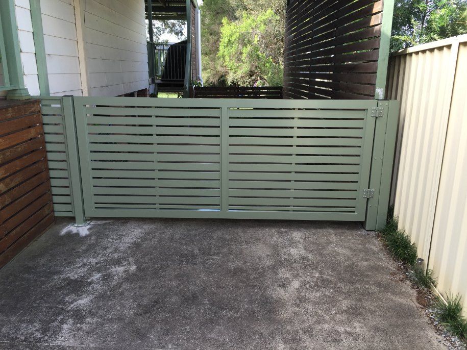 A Green Fence is Sitting in Front of a House — Newcastle & MidCoast Privacy Screens & Gates In Maitland, NSW