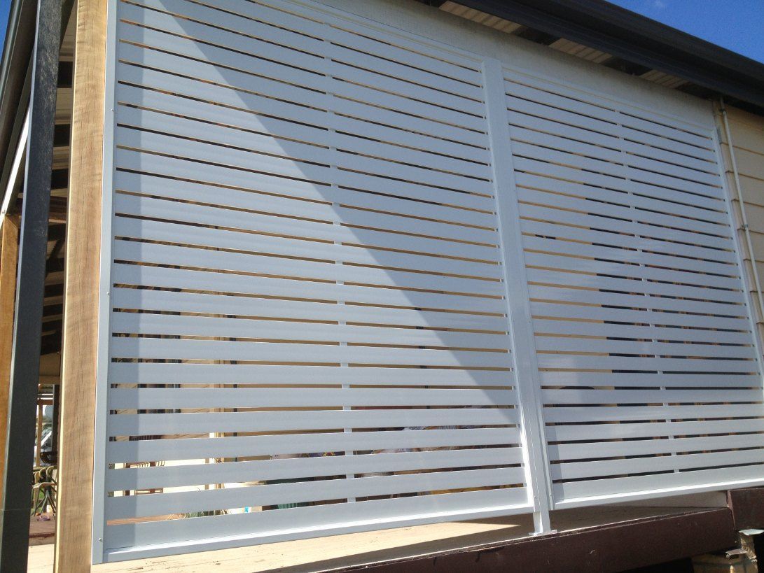 A White Fence is Sitting on the Side of a Building — Newcastle & MidCoast Privacy Screens and Gates In Maitland, NSW