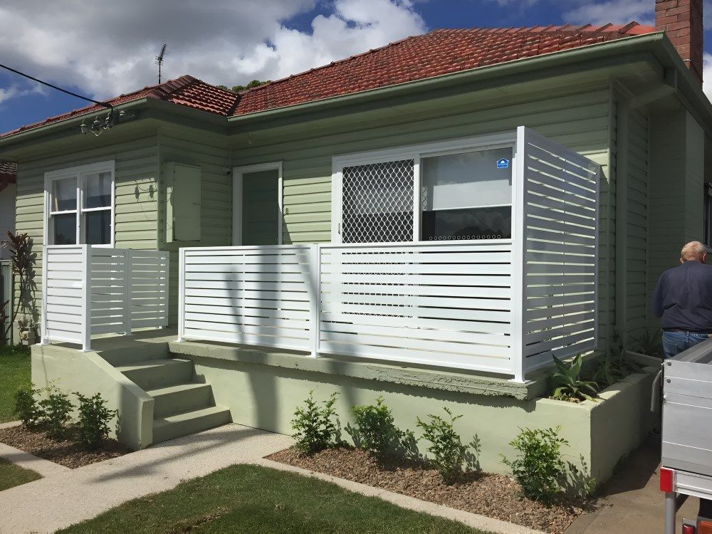 A Man Is Standing In Front Of A House With A White Railing — Newcastle & MidCoast Privacy Screens & Gates In Newcastle, NSW