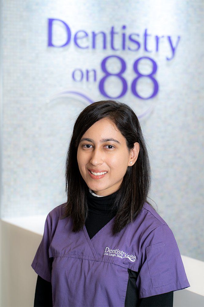 Smiling dental staff member in purple scrubs standing in front of a Dentistry on 88 sign