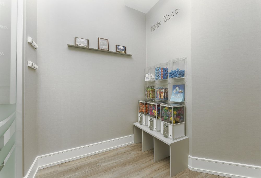 Small gray waiting room with a shelf of product samples and framed items on the wall.