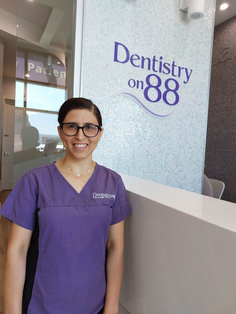 Woman in purple scrubs standing at Dentistry on 88 reception area, smiling.