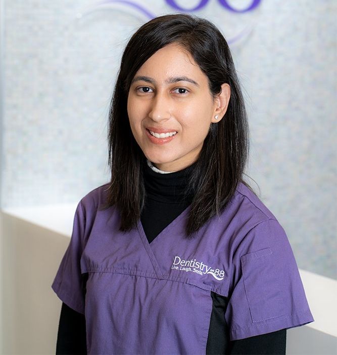 Portrait of a smiling healthcare worker in purple scrubs against a softly lit clinic background