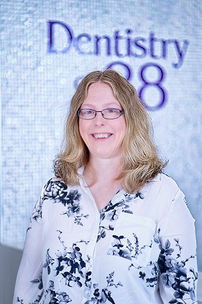 Portrait of a smiling woman in glasses standing before a “Dentistry 88” sign
