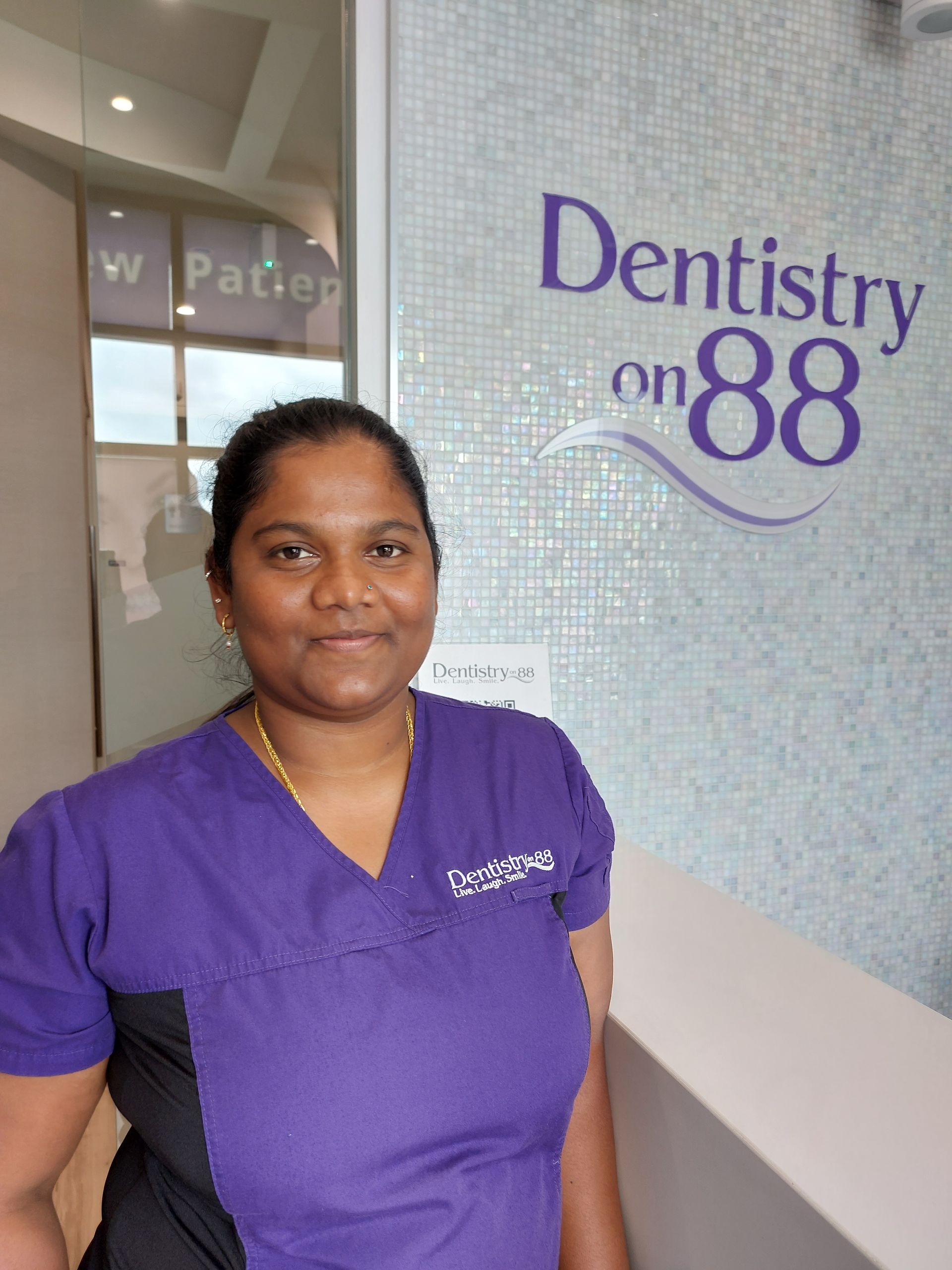 Woman in purple scrubs standing beside a Dentistry on 88 sign.