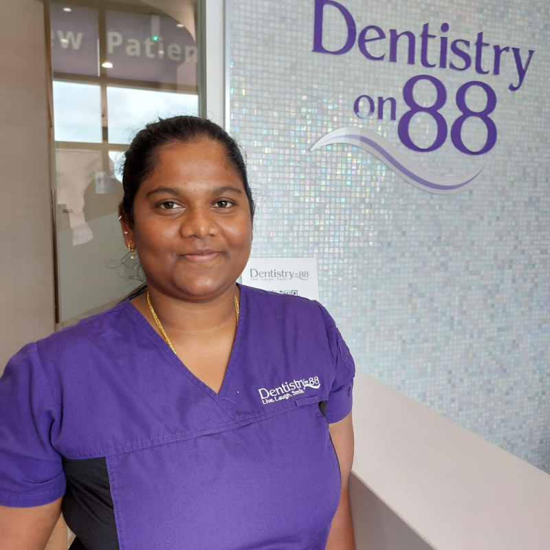 Woman in purple scrubs standing in a dental office beside a “Dentistry on 88” sign