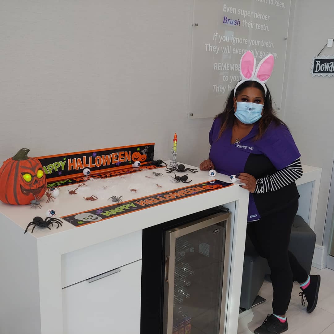 Person in a mask and pink bunny ears stands beside a Halloween-decorated counter.