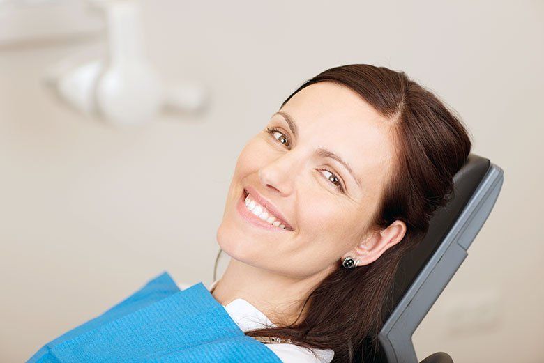 Smiling woman reclining in a dental chair with a blue bib in a bright clinic