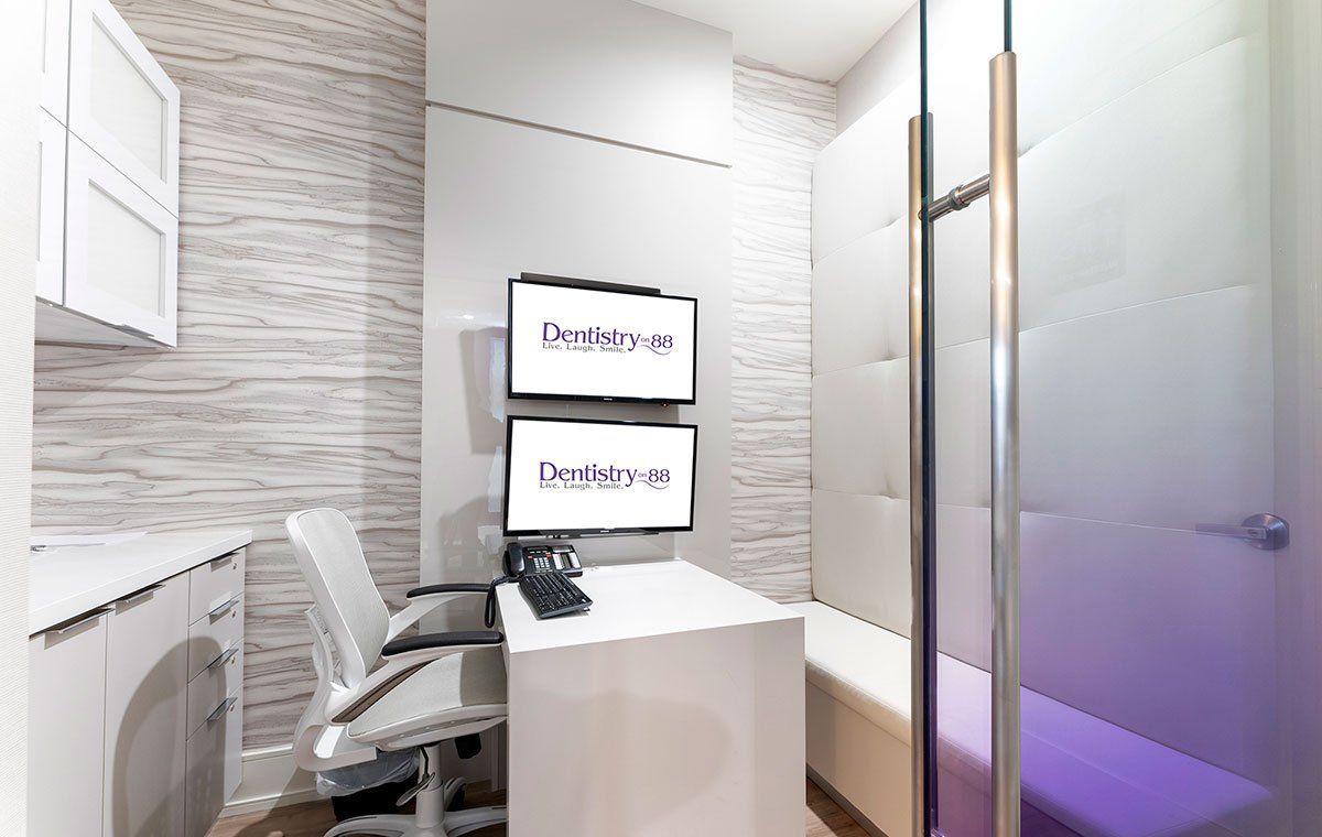 Modern treatment room with chair, two monitors, and glass partition with purple light
