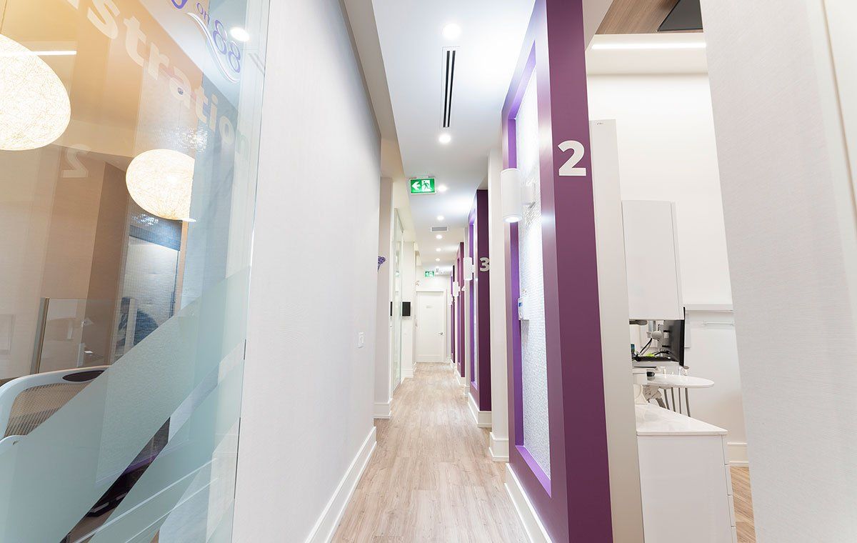 Bright office hallway with purple accents, glass partitions, and numbered rooms