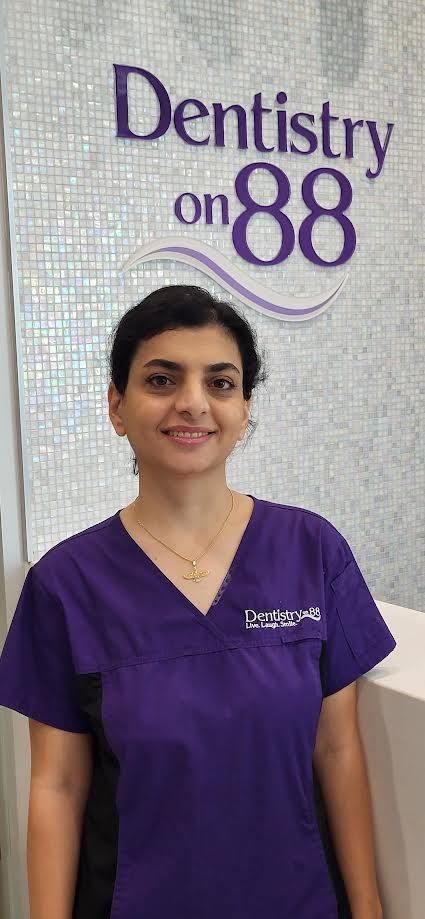 Smiling dental staff member in purple scrubs standing before a Dentistry ’88 sign.