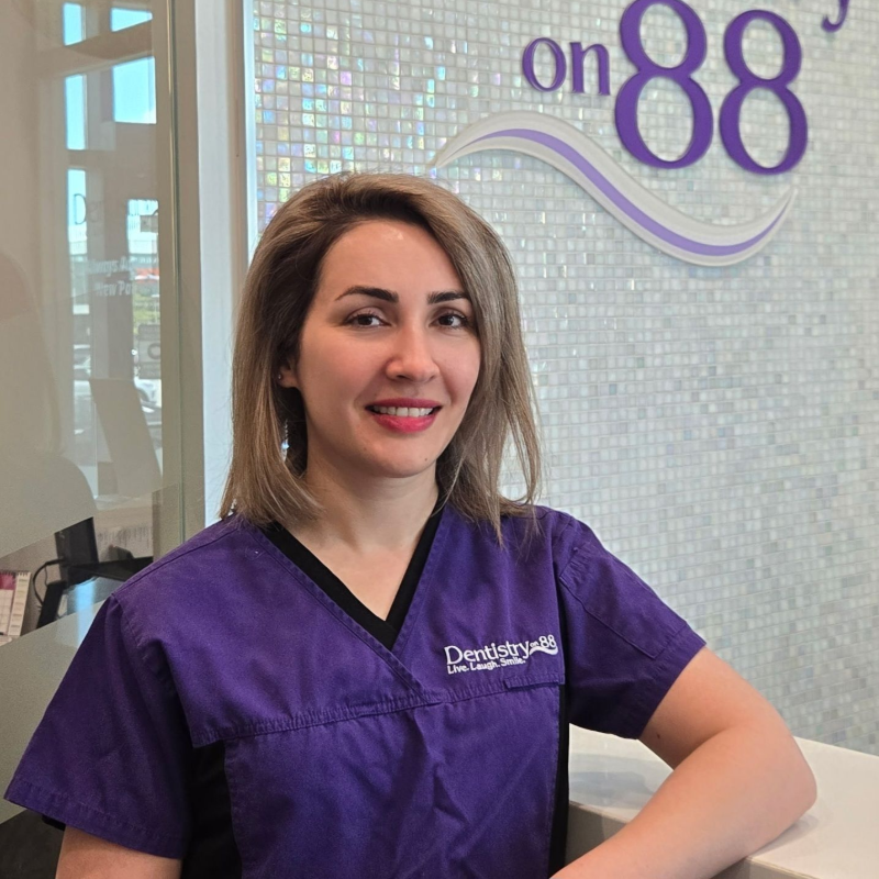 Woman in purple scrubs smiling at a dental clinic reception desk