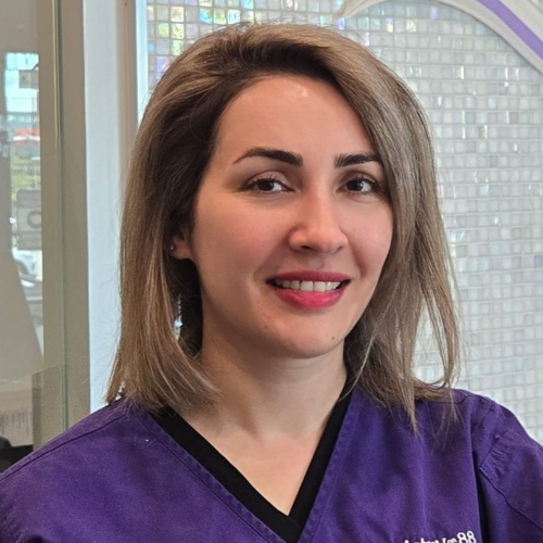 Portrait of a smiling person in a purple top indoors, with a windowed background