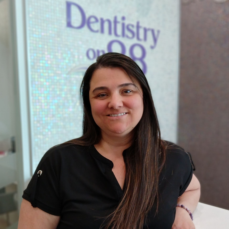 Woman smiling in a black top, standing in front of a Dentistry sign.