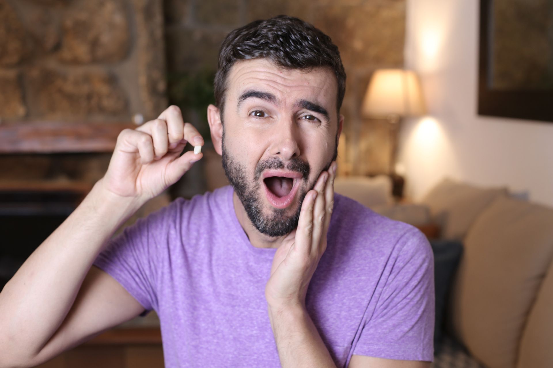 Smiling man in a purple shirt making a surprised gesture in a living room