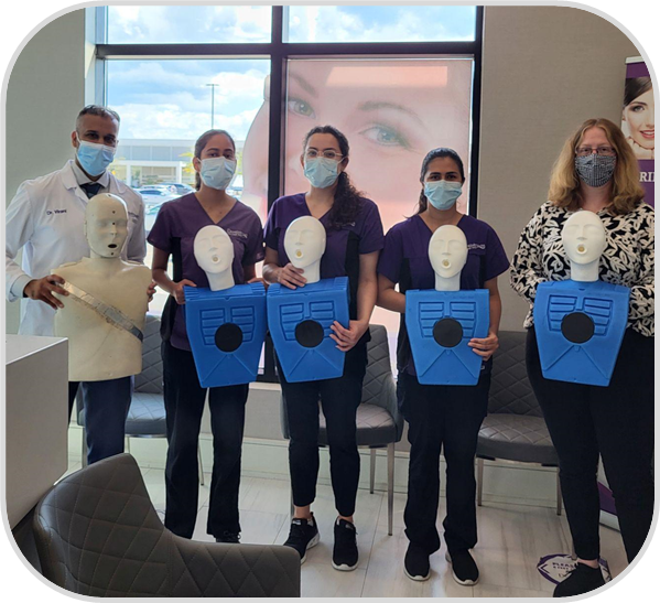 People posing indoors holding blue certificates with masks on, in front of a large window